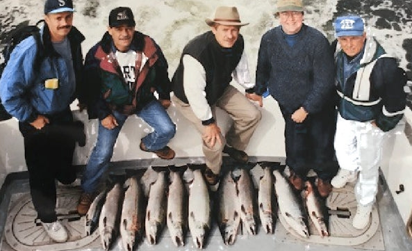 Group of men standing in front of fish on a boat.